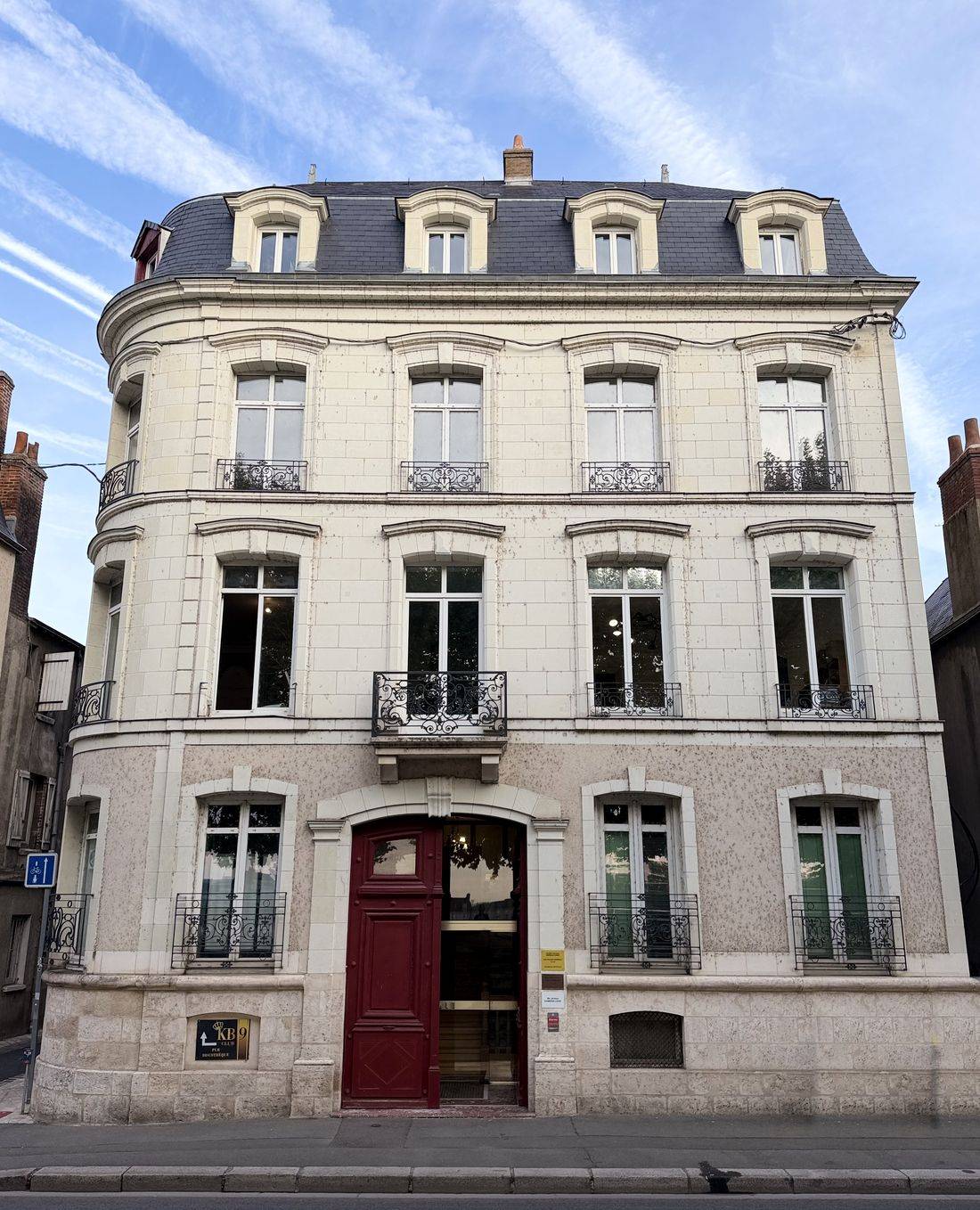 Façade du 8 quai Saint-Jean à Blois : immeuble d'angle en pierre claire à toit d'ardoise, avec une haute porte cochère bordeaux.